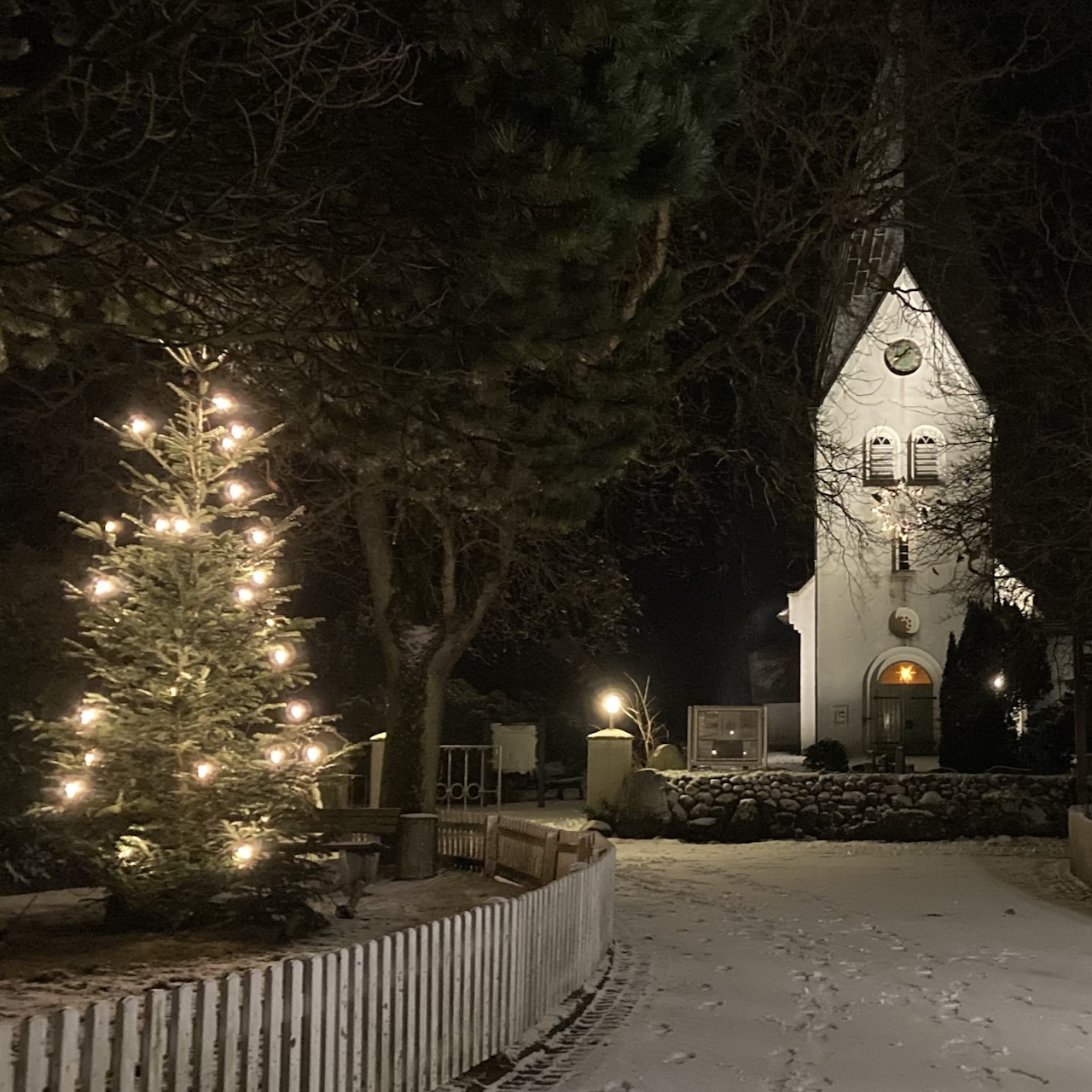 die verschneite St.-Clemens-Kirche in Nebel auf Amrum mit einem beleuchteten Weihnachtsbaum davor